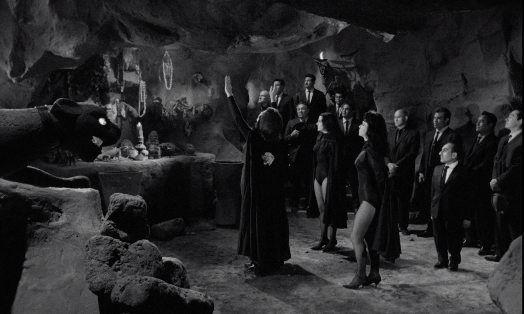 Black and white still of a cult worshipping at a panther-themed altar